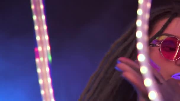 Porträt eines Mädchens mit Dreadlocks in Neon UF Light. Model Girl tanzen mit einer geliehenen LED ist rote Sonnenbrille, Art Design der weiblichen Disco-Tänzerin Modell in UV, bunte abstrakte Make-up. — Stockvideo