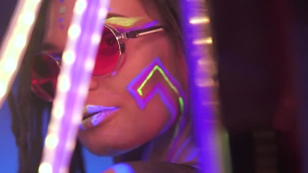 Retrato de uma menina com Dreadlocks em Neon UF Light. Modelo menina dançando com um LED emprestado é óculos de sol vermelhos, Design de arte do modelo de dançarina de disco feminino em UV, maquiagem abstrata colorida . — Vídeo de Stock