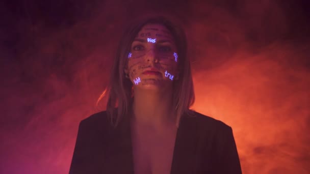 Κορίτσι σε ομίχλη και δραματικό ζεστό φως με γραπτές διαφορετικές λέξεις στο πρόσωπό της. Όμορφο μοντέλο με UV Fluorescent neon δημιουργικό make-up. πρόσωπο κοντά — Αρχείο Βίντεο