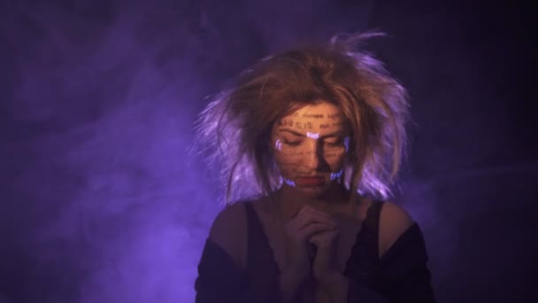 Flicka i dimma och dramatisk lila ljus med skrivna olika språk ord på ansiktet. Vacker modell med UV Fluorescerande neon kreativ make-up. ansikte på nära håll — Stockvideo