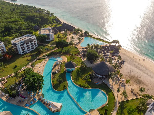 Vista aérea de piscina, sombrillas, playa de arena con palmeras verdes. Costa del océano Índico al atardecer en verano. Zanzíbar, África. Vista superior. Paisaje con agua azul, sombrillas, palmeras. Lujo — Foto de Stock