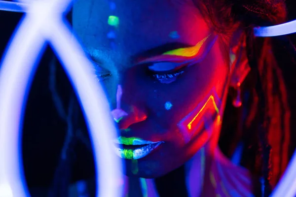 Porträtt av en tjej med glödande rör i Neon UF Light. Modellflicka med dreadlocks och fluorescerande kreativ psykedelisk makeup, Art Design of Female Disco Dancer Modell i UV, Färgglada Abstrakt make-up — Stockfoto