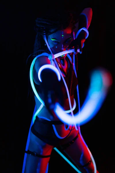 Retrato de uma menina com tubos brilhantes em Neon UF Light. Menina modelo com Dreadlocks e maquiagem psicodélica criativa fluorescente, Design de arte do modelo de dançarina de disco feminino em UV, maquiagem abstrata colorida — Fotografia de Stock