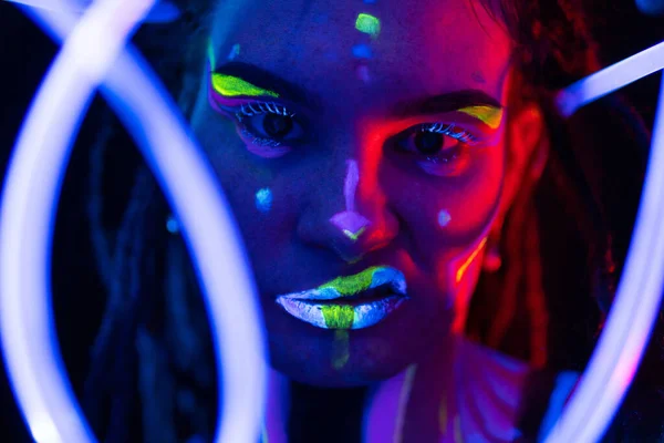 Retrato de uma menina com tubos brilhantes em Neon UF Light. Menina modelo com Dreadlocks e maquiagem psicodélica criativa fluorescente, Design de arte do modelo de dançarina de disco feminino em UV, maquiagem abstrata colorida — Fotografia de Stock