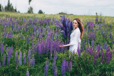 Beyaz elbiseli bir kız lupines arasında duruyor