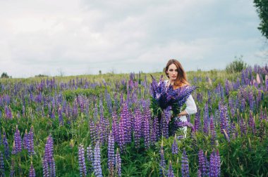 Beyaz elbiseli bir kız lupines arasında duruyor