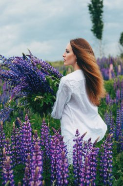 Beyaz elbiseli bir kız lupines arasında duruyor