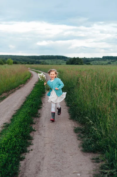 Ένα χαρούμενο παιδί λειτουργεί με ένα μπουκέτο μαργαρίτες σε μπότες — Φωτογραφία Αρχείου