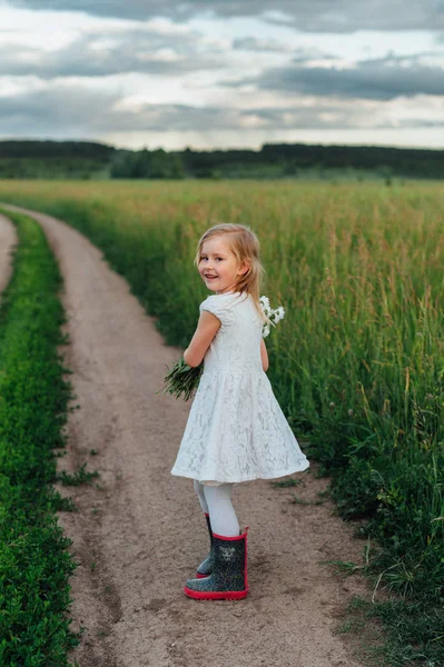 Bambino sul sentiero con un mazzo di camomille in stivali — Foto Stock