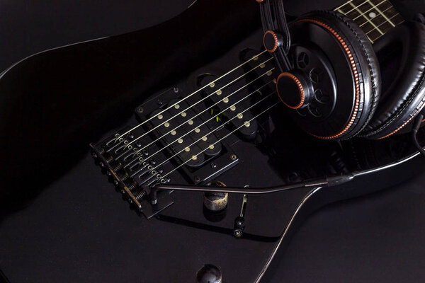Headphone on black electric guitar in darkness.