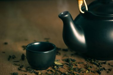 Bardak çay sıcak duman ile seramik çaydanlık yerleştirilir ve kuru çay ahşap arka plan üzerinde dağınık bırakır.