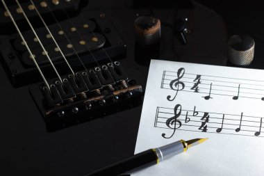 Karanlıkta siyah elektro gitarda müzik notası ve klasik kalem. Rock müzik yaratıcılığı kavramı.