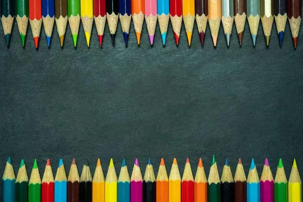 Kara tahta arka planda renkli kalemler. Üst görünüm ve kopya alanı. Sanat eğitimi konsepti.