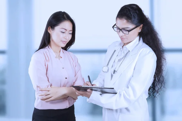 Doctor escribiendo en portapapeles con su paciente — Foto de Stock