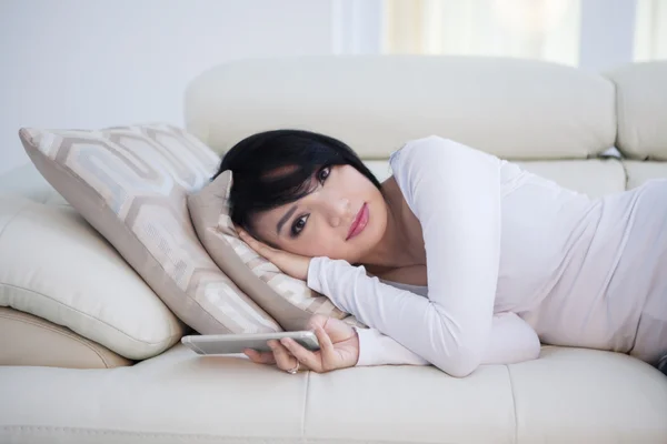 Woman holds smartphone and lying on sofa — Stok fotoğraf