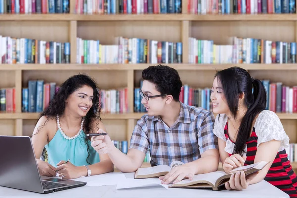 Tre studenti con computer portatile in biblioteca — Foto Stock