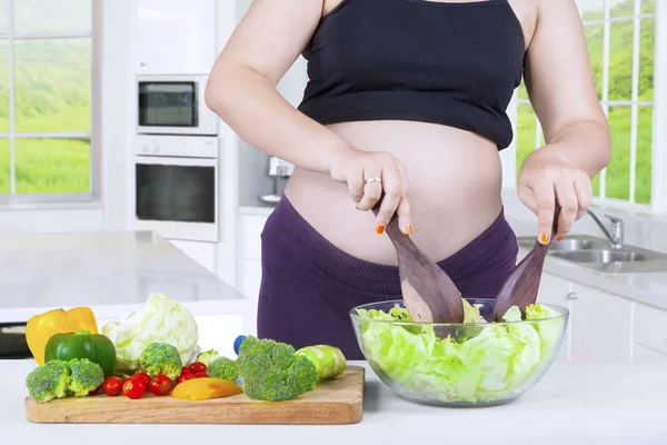 Pregnant mother makes salad on the bowl — Stockfoto