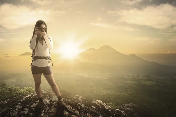 Mujer de pie sobre la roca con una cámara — Foto de Stock