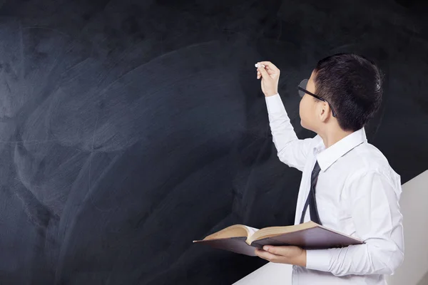 Jongen houdt van boek en schrijft op schoolbord — Stockfoto