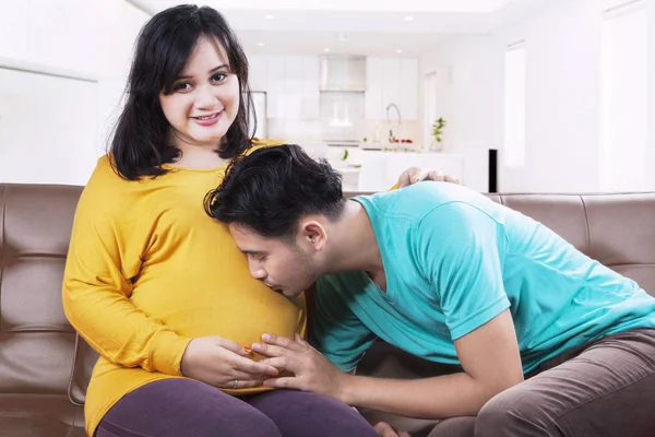 Husband kisses pregnant tummy on sofa — Stock Photo, Image