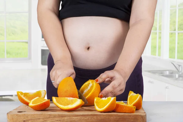 Mulher expectante corta frutas frescas de laranja — Fotografia de Stock