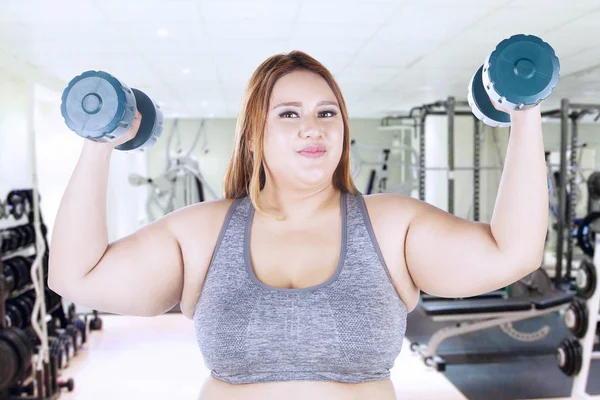 Толстая женщина поднимает гантели в спортзале — стоковое фото