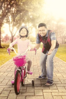 Küçük kız babasıyla bisiklet sürmeyi öğreniyor.