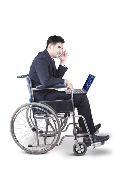 Businessman with laptop and wheelchair on studio — Stock Photo, Image