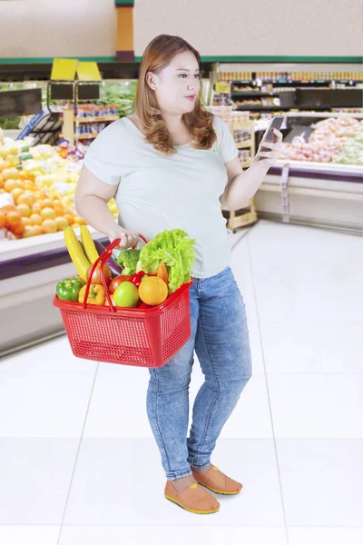 Dicke Frau tippt im Supermarkt auf Smartphone — Stockfoto