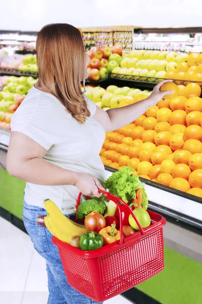 Överviktig kvinna tar orange i livsmedelsbutiker — Stockfoto