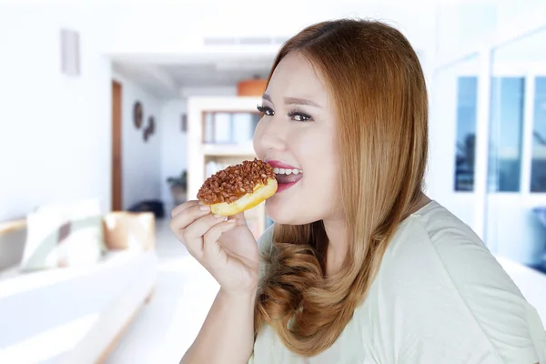 Όμορφη γυναίκα τρώει ντόνατ στο σπίτι — Φωτογραφία Αρχείου