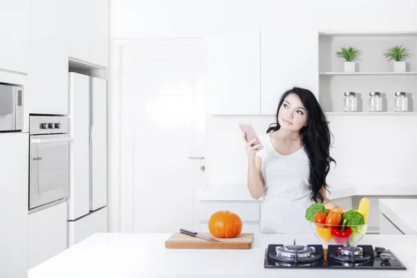 Nadenkend vrouw met smartphone in de keuken — Stockfoto