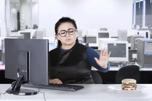 Mujer con computadora y hamburguesa en la oficina — Foto de Stock