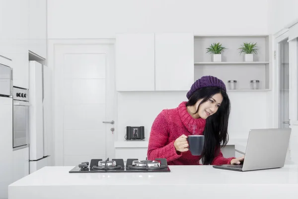 キッチンでセーターとを使用してラップトップを持つ女性 — ストック写真