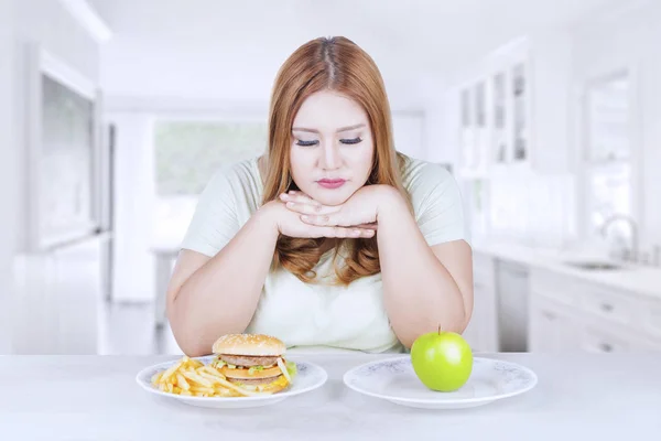Verwirrte Frau wählt Apfel oder Hamburger — Stockfoto