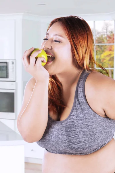 Толстая женщина ест яблоко на кухне — стоковое фото