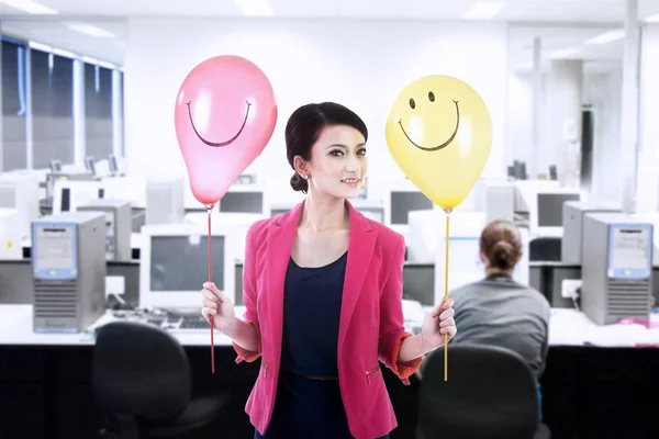 Empresária segurando balões felizes no escritório — Fotografia de Stock