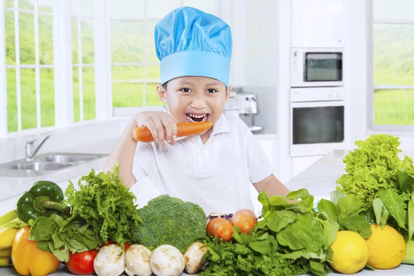 Aranyos fiú megeszi a sárgarépát, a konyhában — Stock Fotó