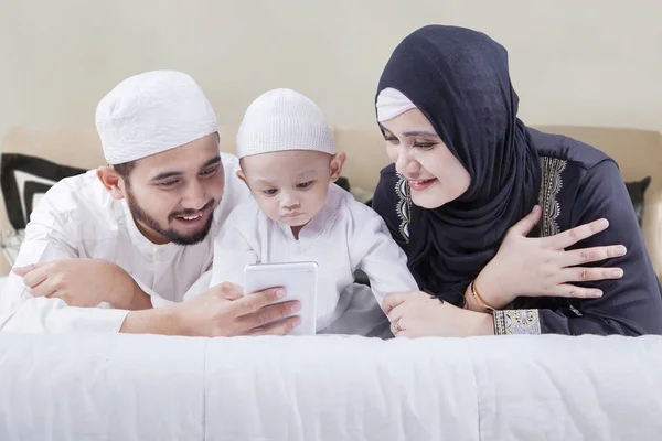 Família muçulmana deitada na cama com smartphone — Fotografia de Stock