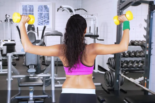 Jeune femme levant haltères à la salle de gym — Photo