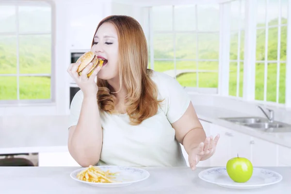 Mujer rubia comiendo hamburguesa en la cocina — Foto de Stock