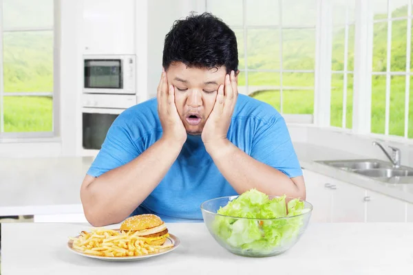Confused man choosing salad or hamburger — Stock Photo, Image