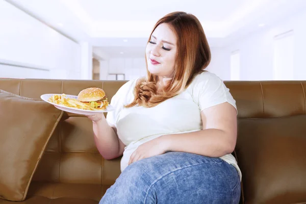 Товста жінка дивиться на їжу на дивані — стокове фото