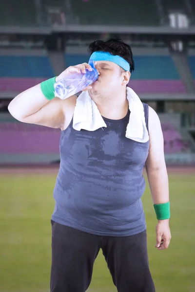 Жирний чоловік п'є на стадіоні — стокове фото