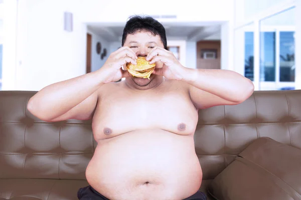 肥満男性の上半身裸のハンバーガーを家で食べる — ストック写真