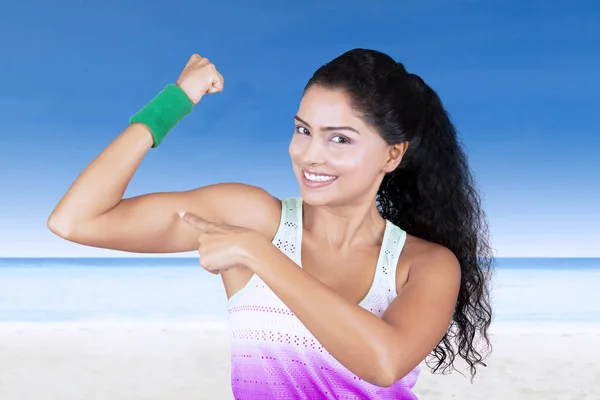 Mujer hermosa señalando músculo en la playa —  Fotos de Stock