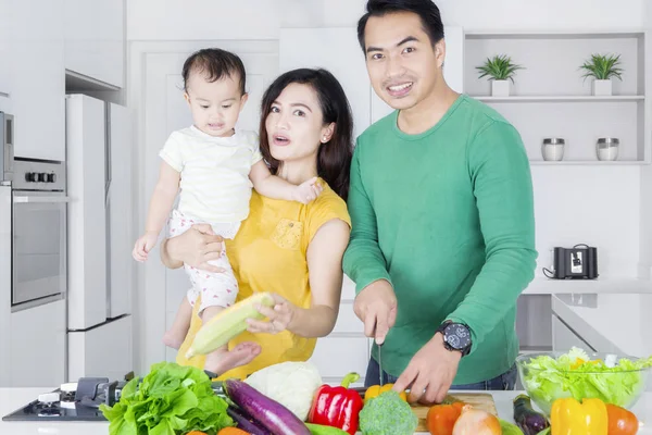 Sonrientes padres y niña cocinan verduras —  Fotos de Stock