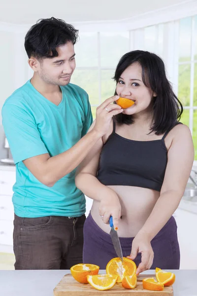Pareja joven comiendo naranja en la cocina — Foto de Stock
