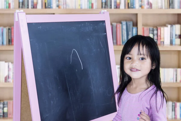 Liten flicka med svarta tavlan i biblioteket — Stockfoto