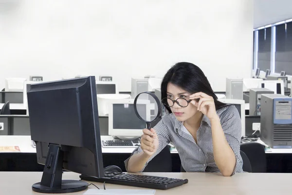Женщина смотрит на компьютер с увеличительным стеклом — стоковое фото